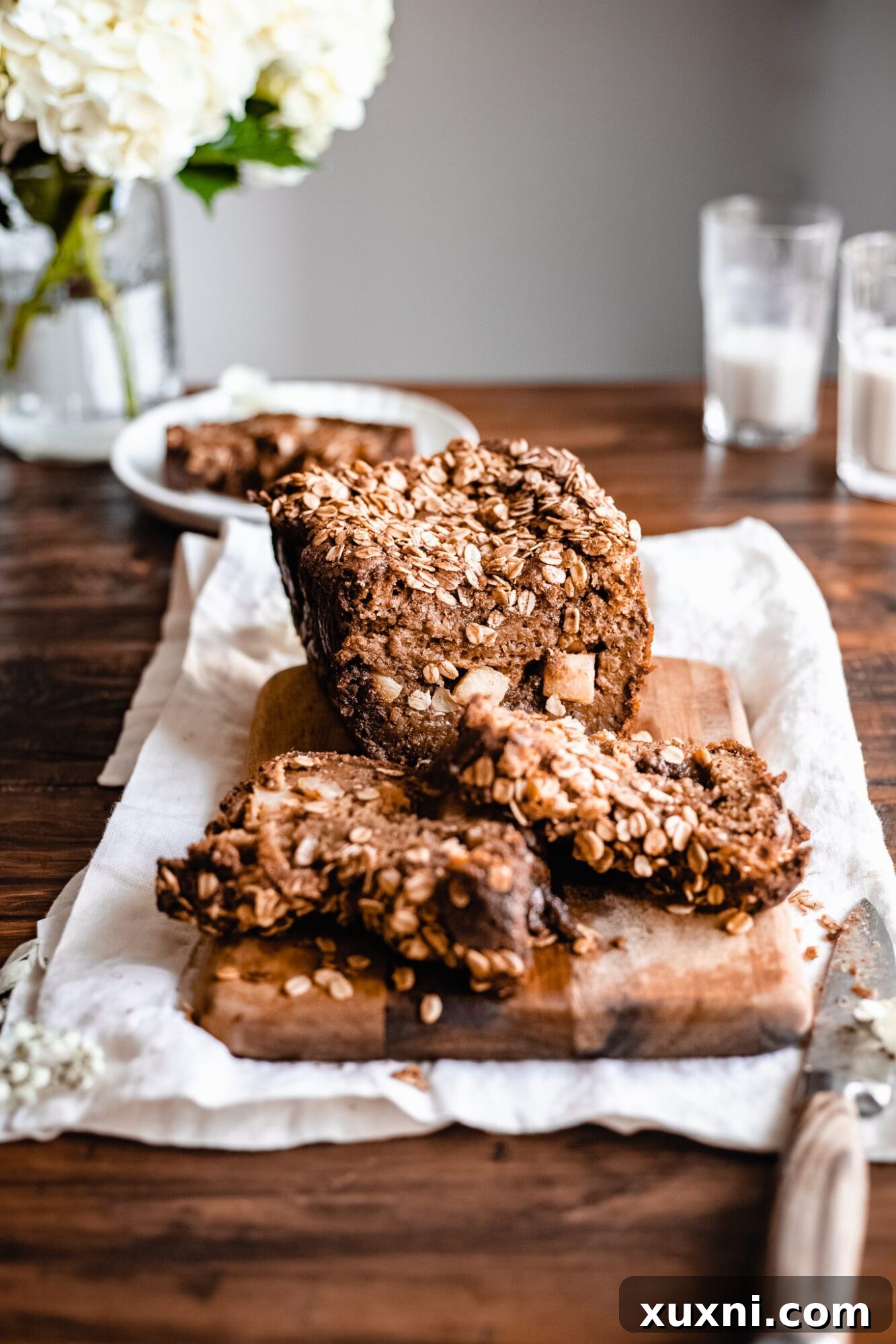 Sliced vegan apple cinnamon bread on a rustic wooden board, garnished with fresh apple slices and cinnamon sticks.