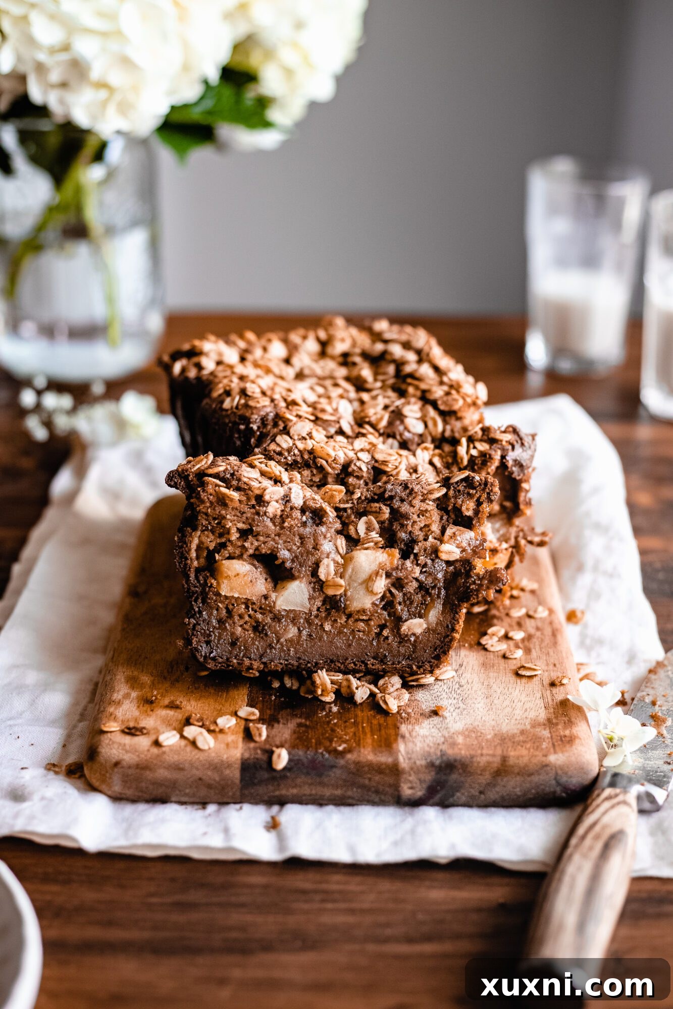 Several thick slices of healthy vegan apple cinnamon bread, showcasing the layers of moist bread, apple filling, and oat crumble, leaning against each other on a wooden surface.