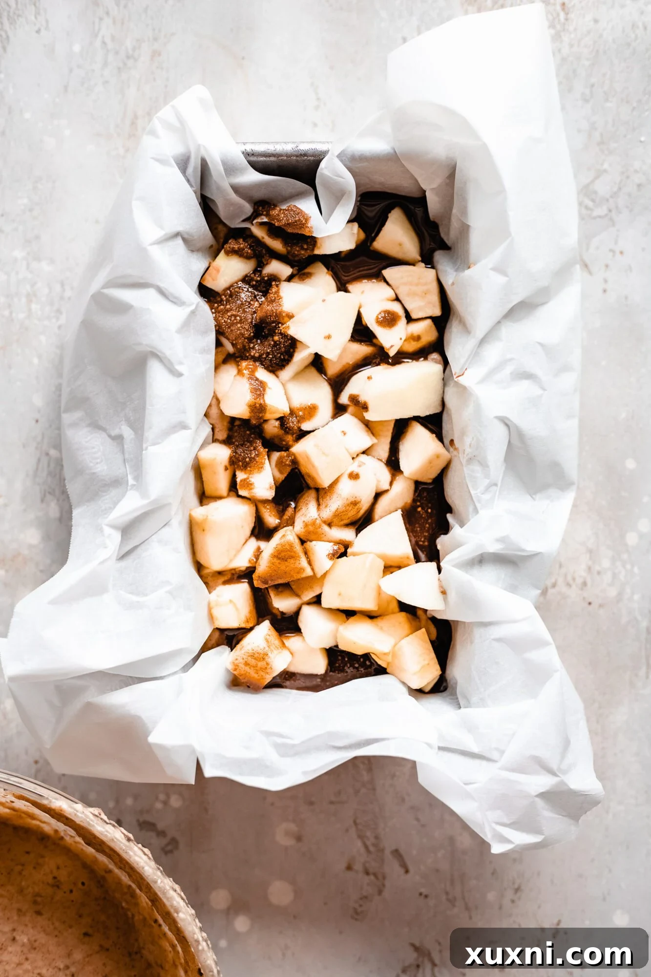 Vegan apple bread batter in a loaf pan with chunks of fresh apples and cinnamon streusel layered inside, ready for the final batter.
