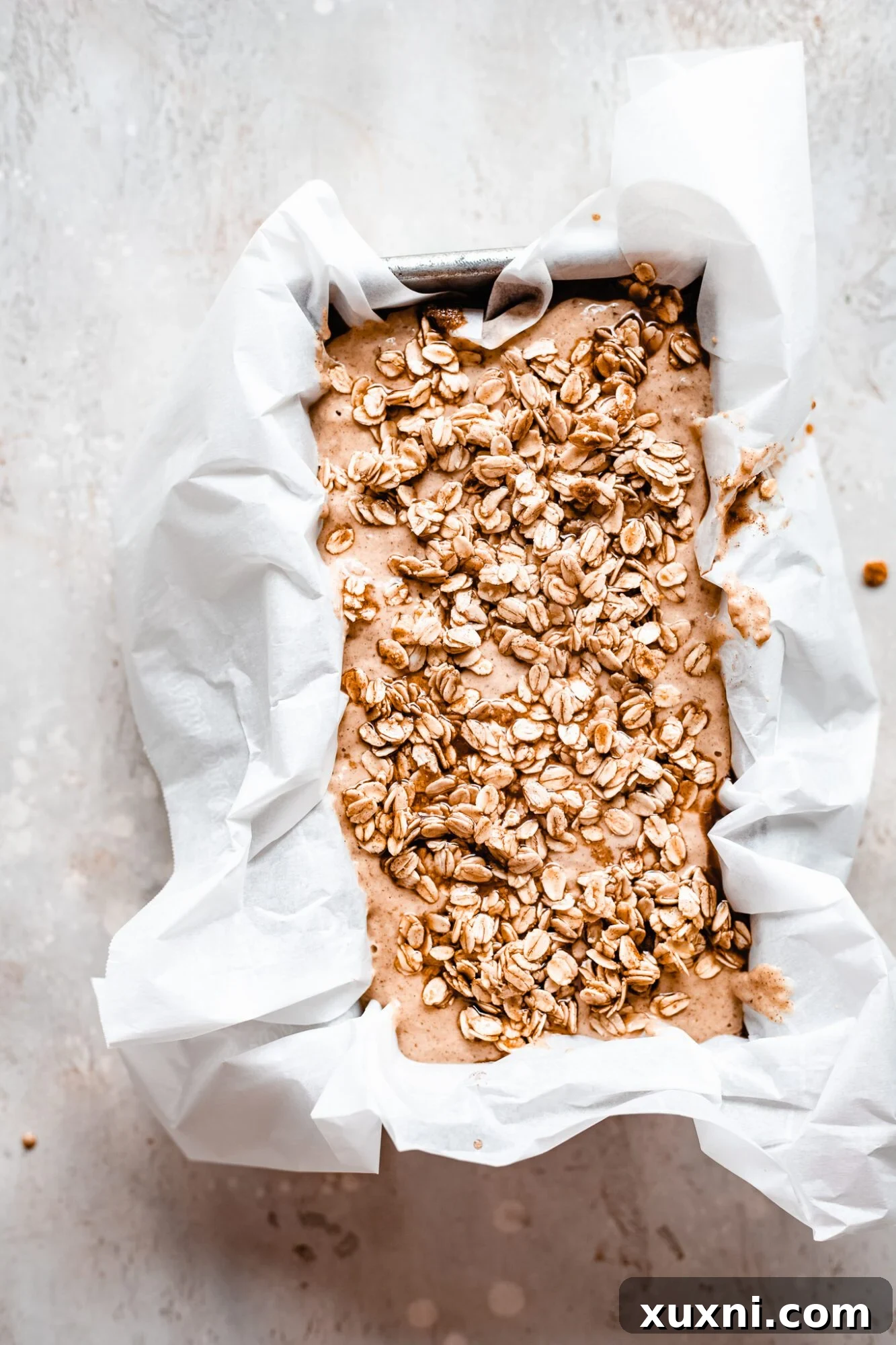 Unbaked vegan apple cinnamon bread in a loaf pan, generously topped with a homemade cinnamon oat crumble, ready for the oven.