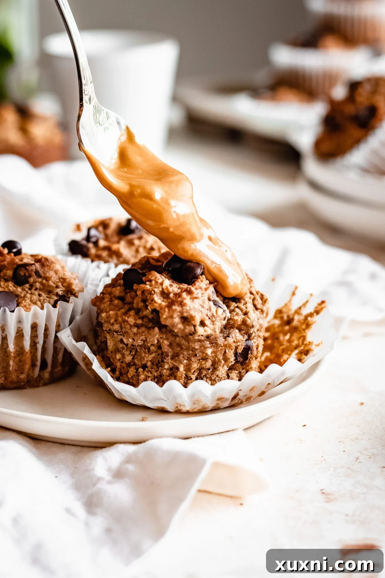 A spoon dripping peanut butter onto a warm peanut butter banana muffin
