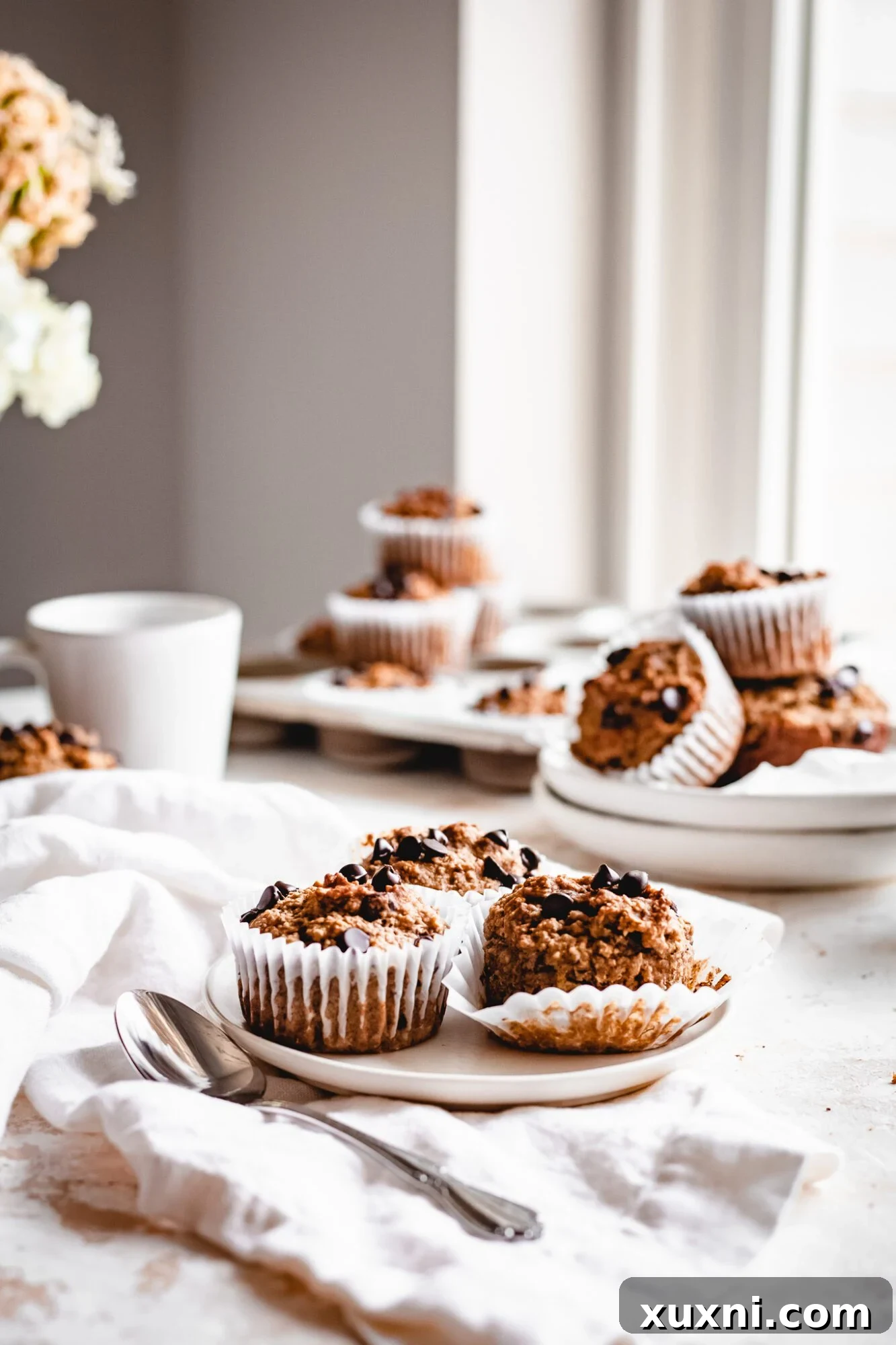 Healthy peanut butter muffins stacked on a plate with more muffins in the background