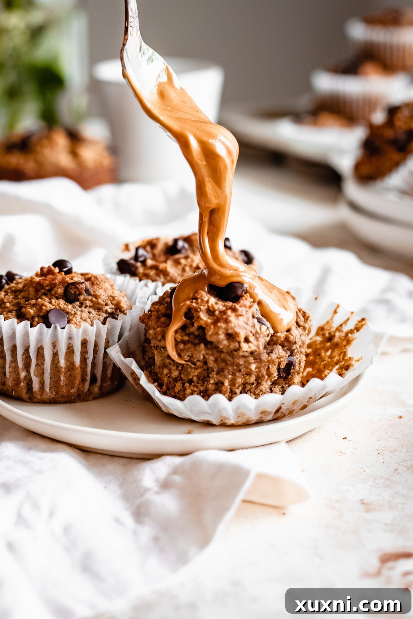 Spoon dolloping creamy peanut butter onto a freshly baked banana muffin