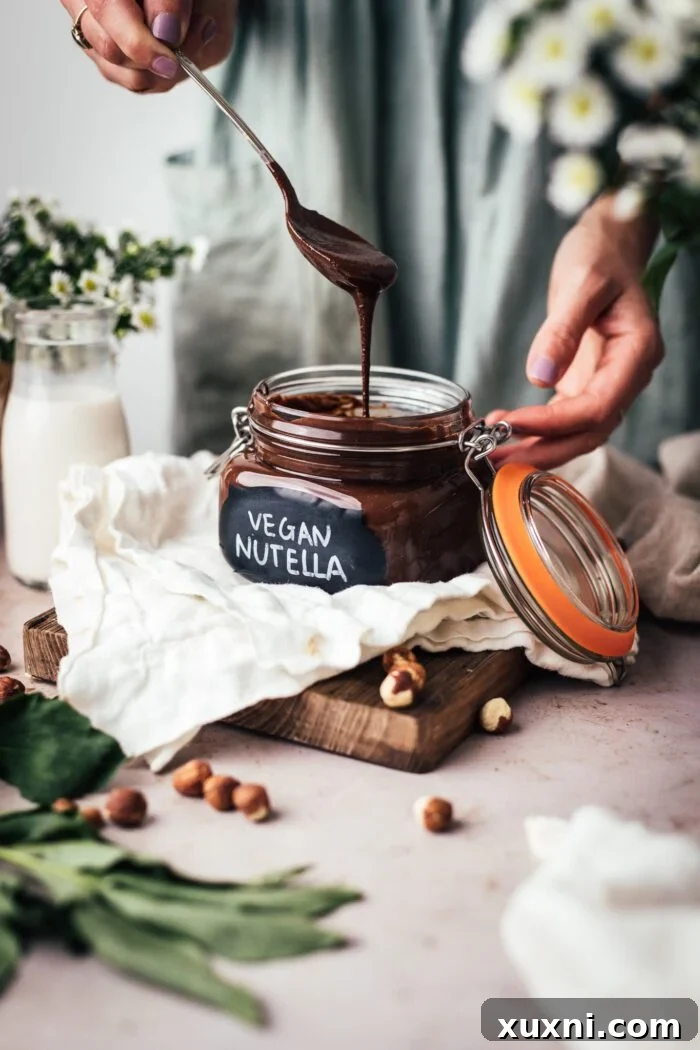 A hand drizzling homemade vegan Nutella into a clean glass jar, showcasing its smooth texture.