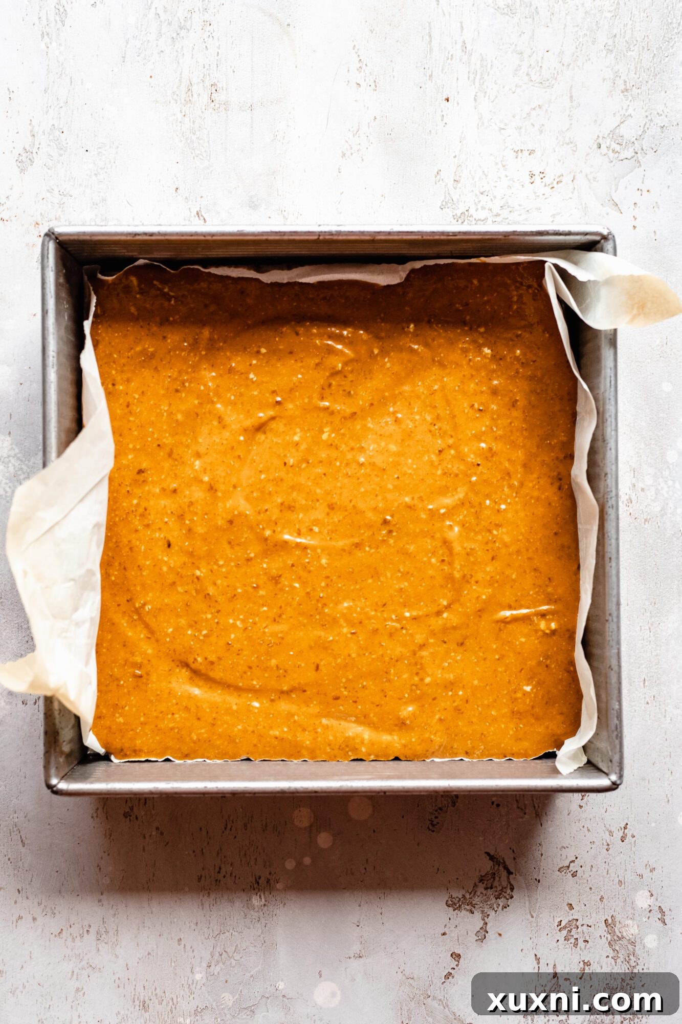 Unbaked pumpkin pie bars, with the creamy filling spread over the crust, poised for baking in the oven.