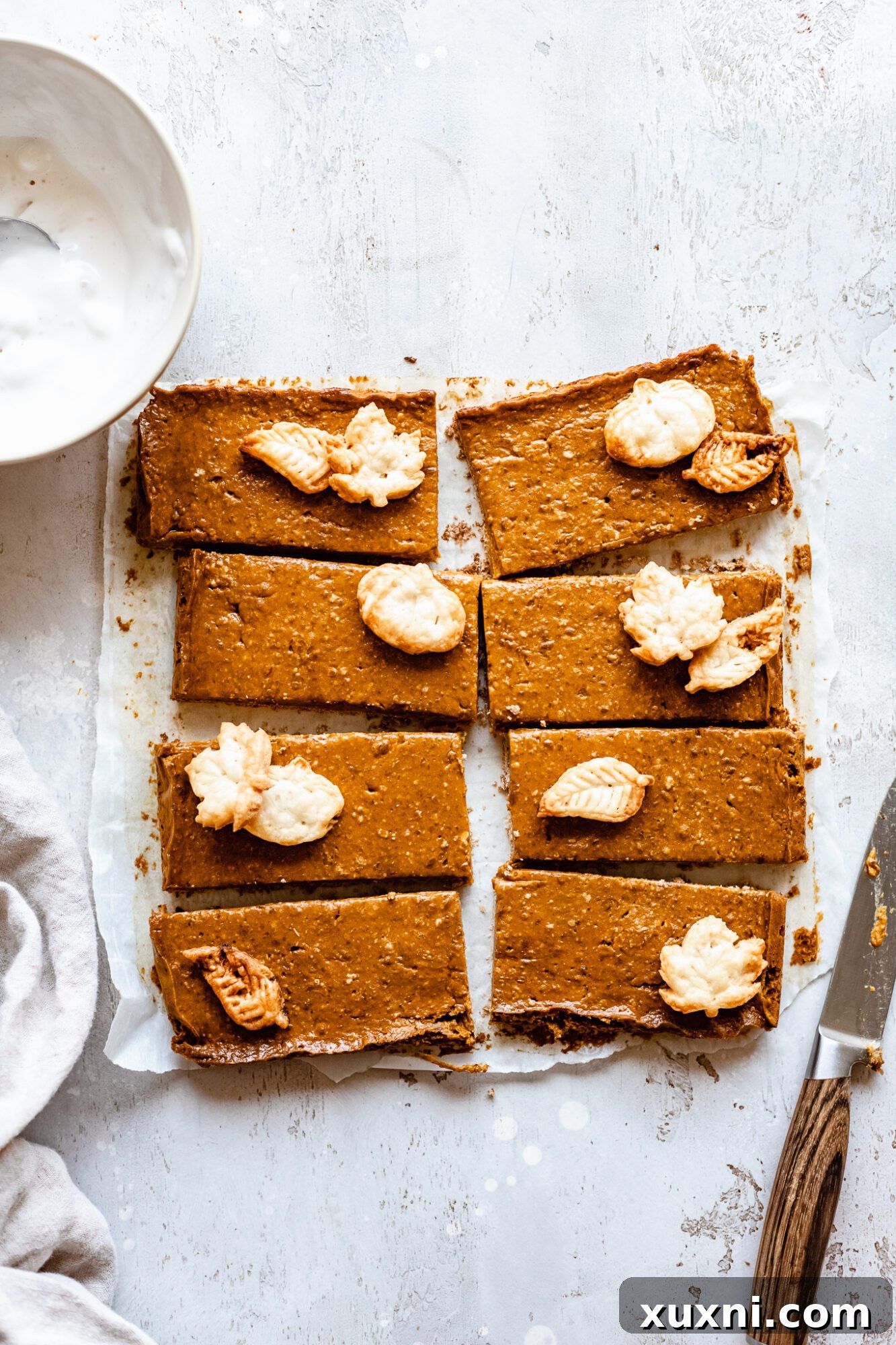 Slices of pumpkin pie bars adorned with small decorative pie crust cut-outs, emphasizing a festive and delightful presentation.