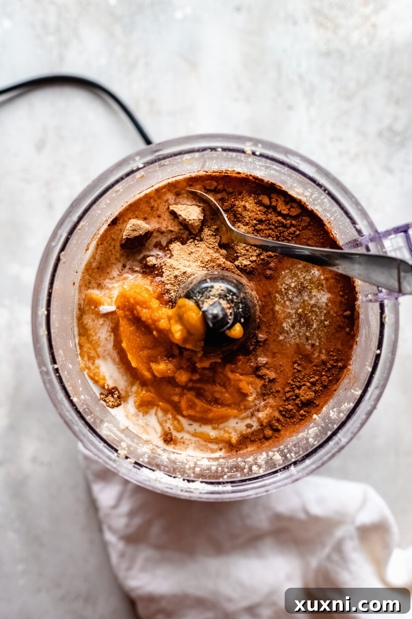 Assorted vegan pumpkin pie filling ingredients, including spices and pumpkin puree, ready for blending.
