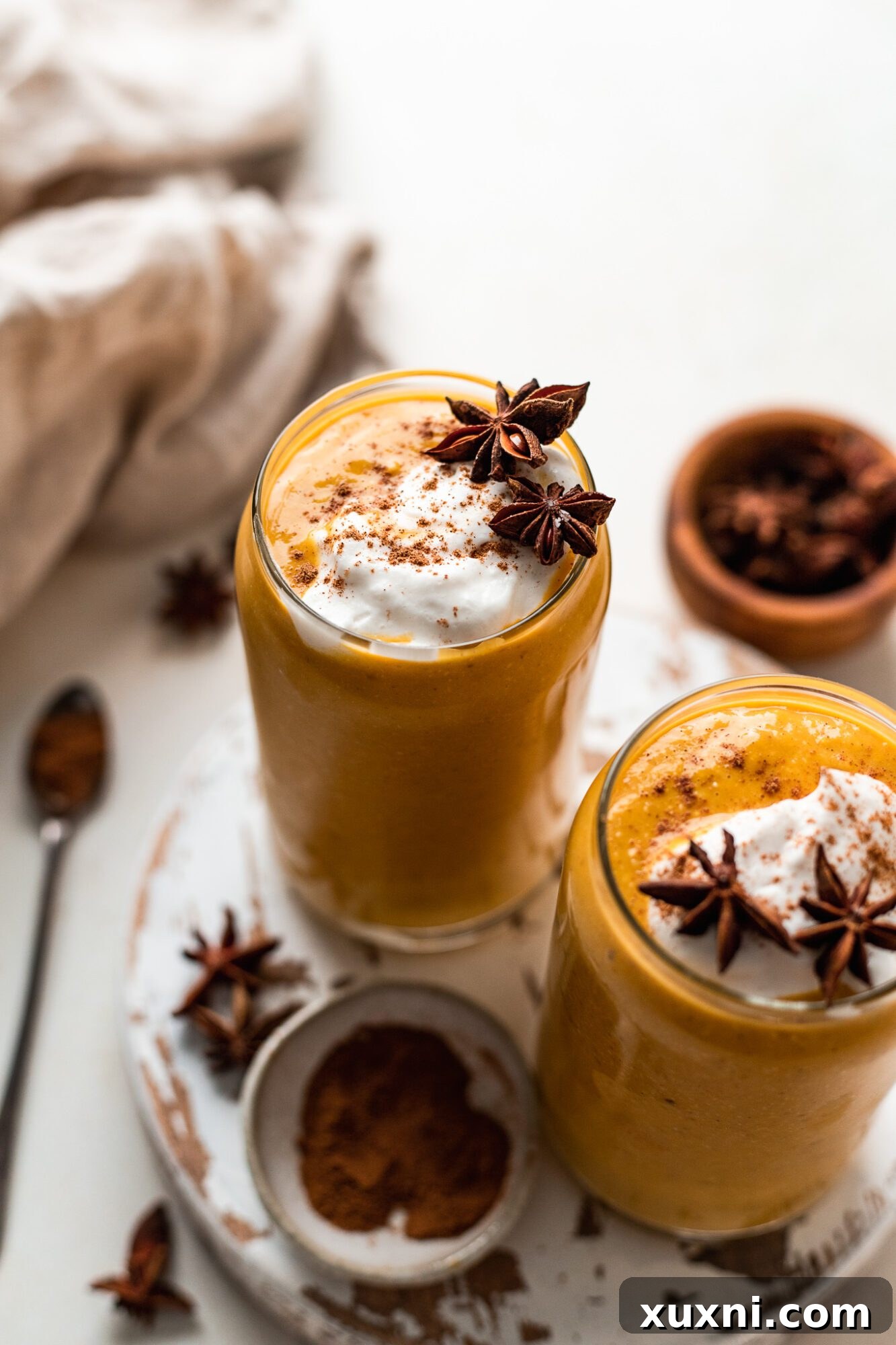 Two glasses of creamy vegan pumpkin pie smoothies garnished with a sprinkle of spice, ready to enjoy.