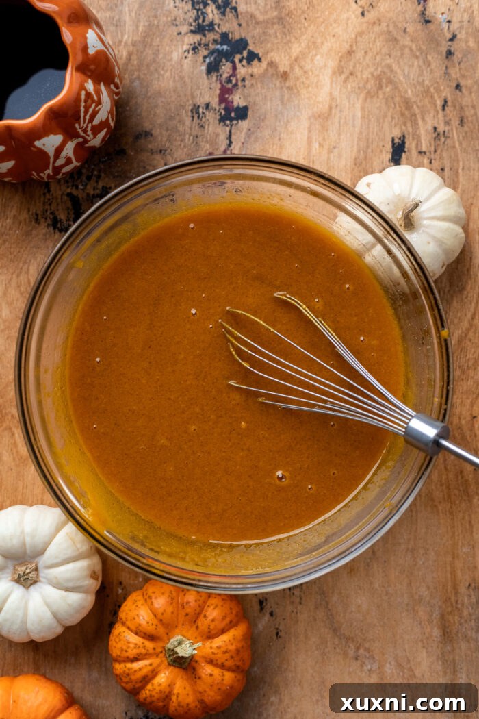 Whisked wet ingredients for vegan pumpkin cake batter in a bowl, showing smooth consistency.