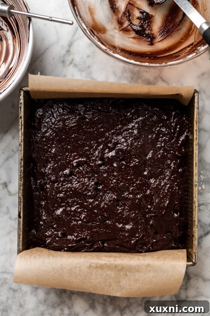 Vegan brownie batter spread evenly in a parchment-lined baking pan, ready for the oven.