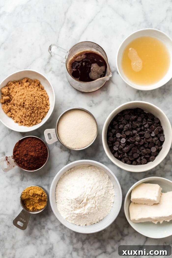 Assortment of vegan brownie ingredients laid out on a white marble surface, including flour, cocoa powder, sugar, and chocolate.