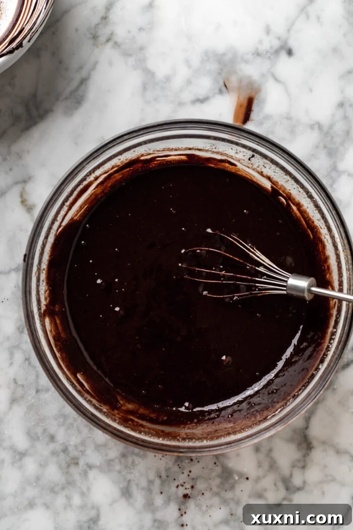Carefully combining the warm chocolate fudge mixture with the dissolved sugar and liquid ingredients to form the brownie batter.