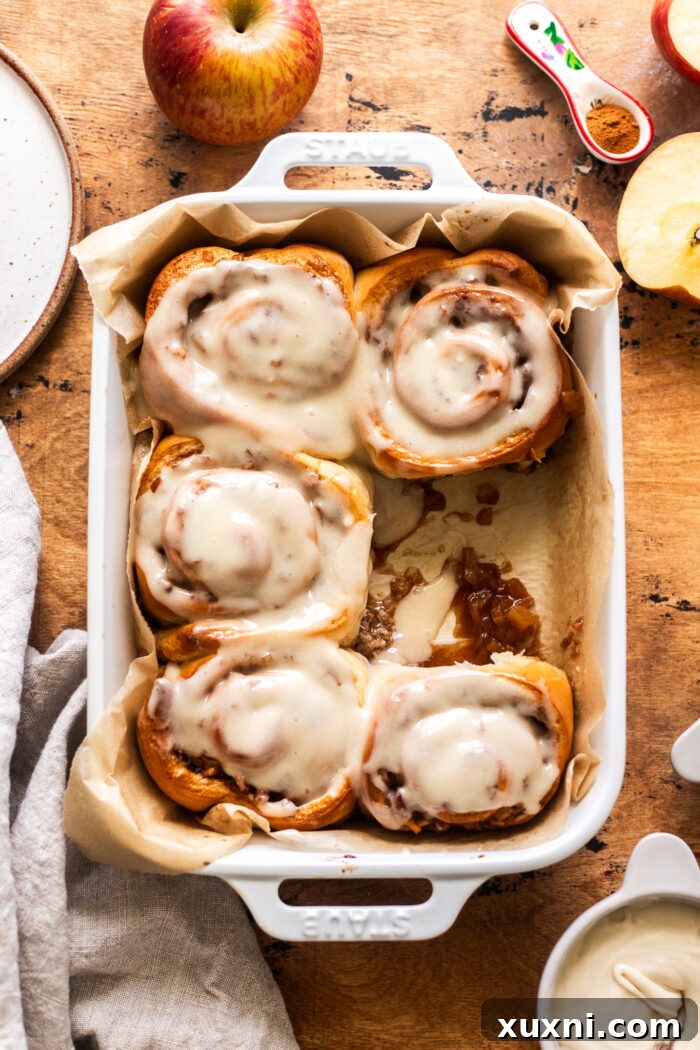 Six golden-brown small batch apple cinnamon rolls in a pan, showcasing their gooey filling and fluffy texture, topped with maple cream cheese frosting.