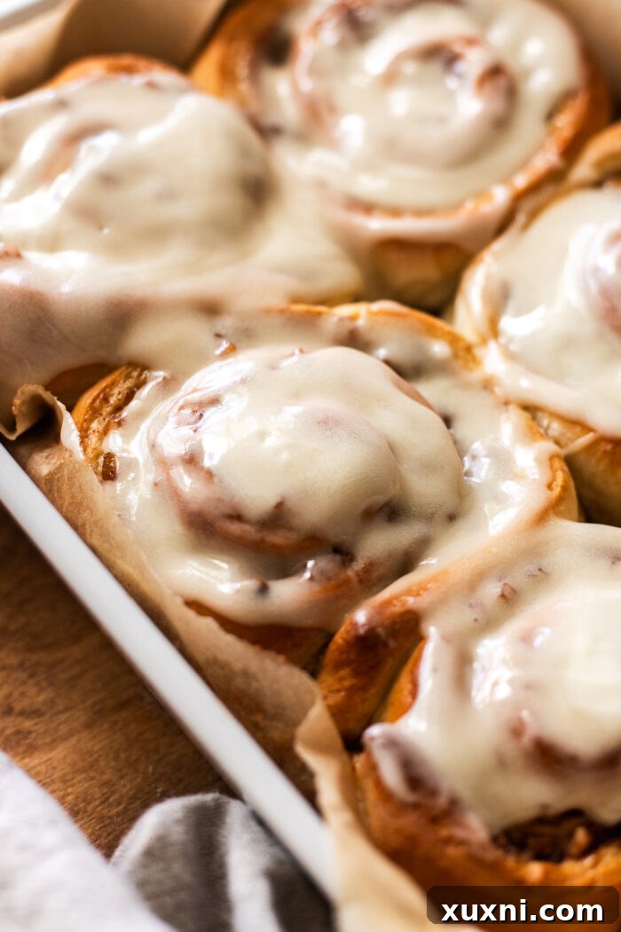 Baked apple cinnamon rolls generously covered with maple cream cheese frosting, ready to be served.
