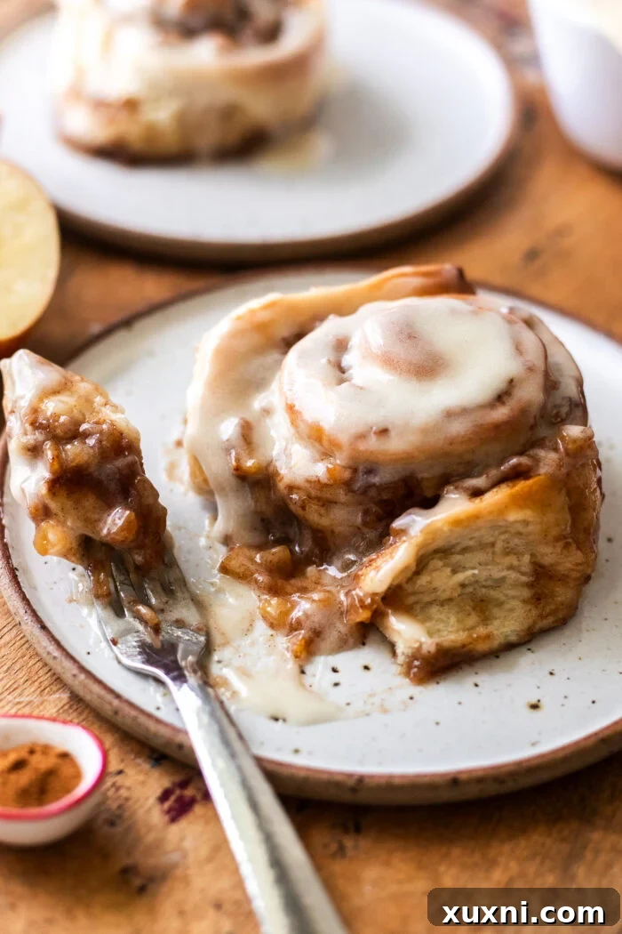 Another close-up of a bitten apple cinnamon roll, highlighting the tender dough, cinnamon sugar swirl, and abundant apple filling, topped with smooth maple frosting.