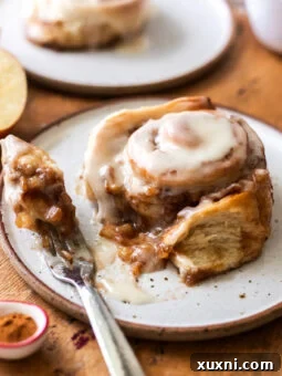 A close-up of a bitten apple cinnamon roll, showing the layers of soft dough, rich apple filling, and generous frosting.