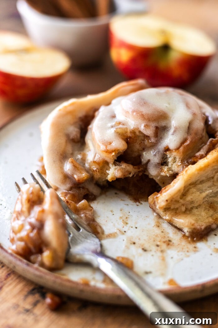 A close-up of a bitten small batch apple cinnamon roll, showing the layers of soft dough, rich apple filling, and generous frosting.