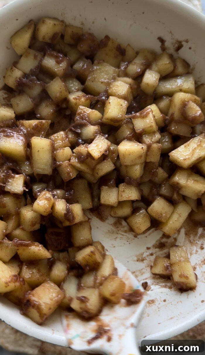 Finely diced apples being sautéed in a skillet with spices, forming the delicious apple pie filling.