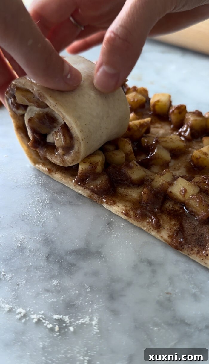 Dough being rolled out and filled with cinnamon sugar and apple pie filling, ready to be sliced.