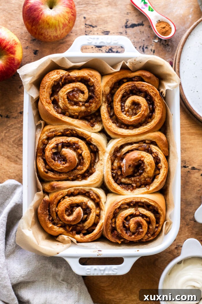 Freshly baked apple cinnamon rolls, golden brown and perfectly puffed, in a baking dish.