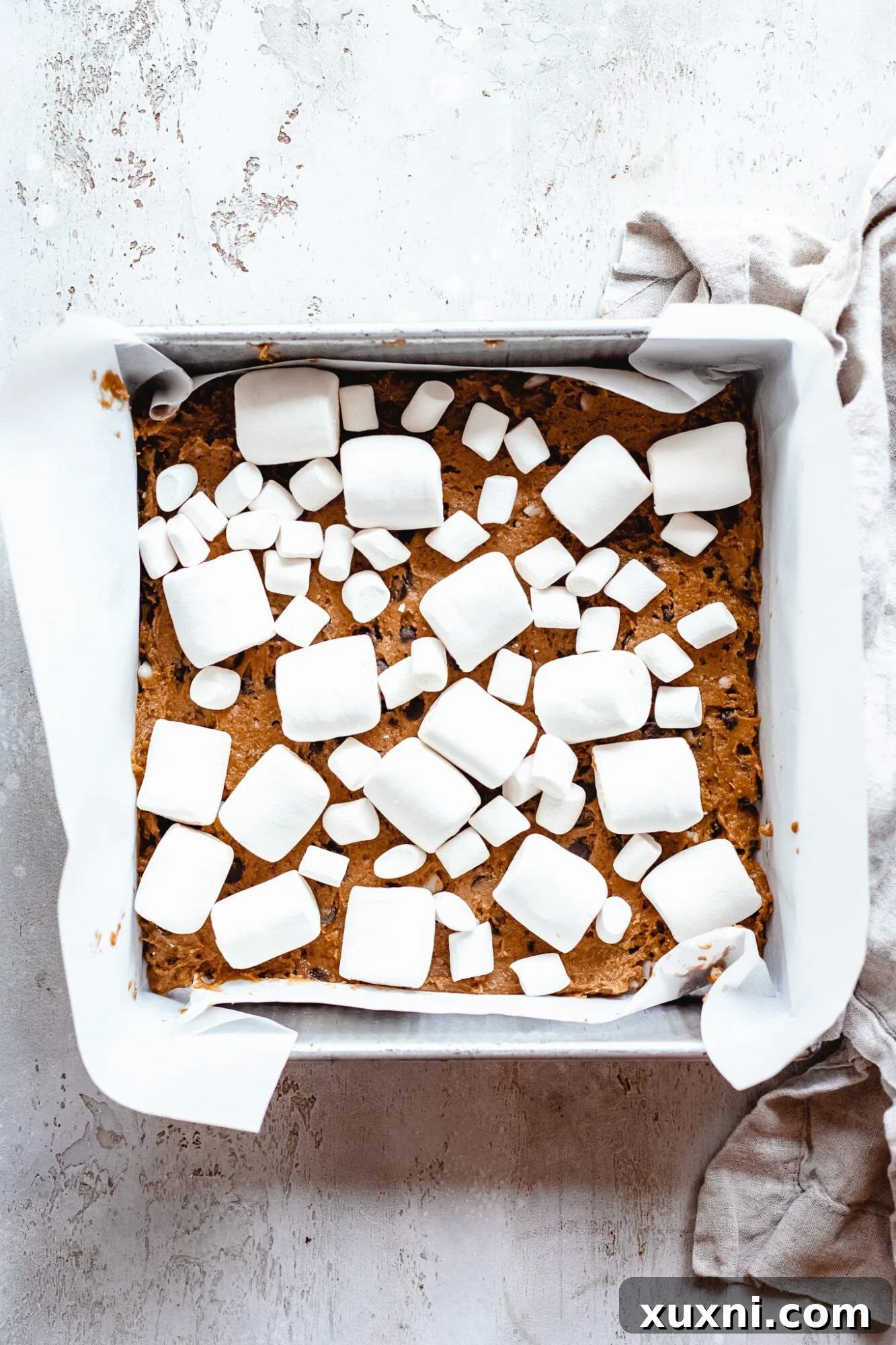 Vegan Smores Brownie Cookie Recipe 8 vegan marshmallows arranged on top of the cookie dough layer in a baking pan