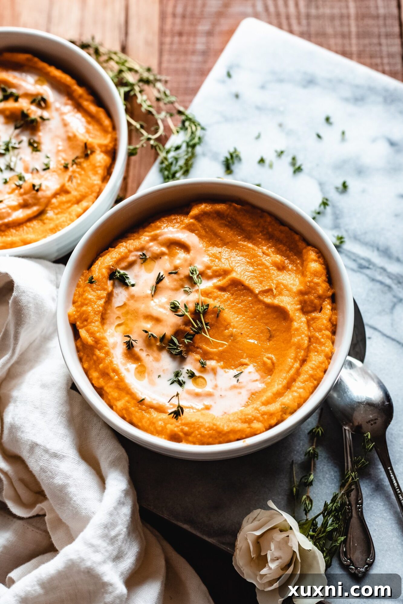 Two bowls of creamy vegan pumpkin sweet potato soup garnished with fresh herbs on a marble surface.