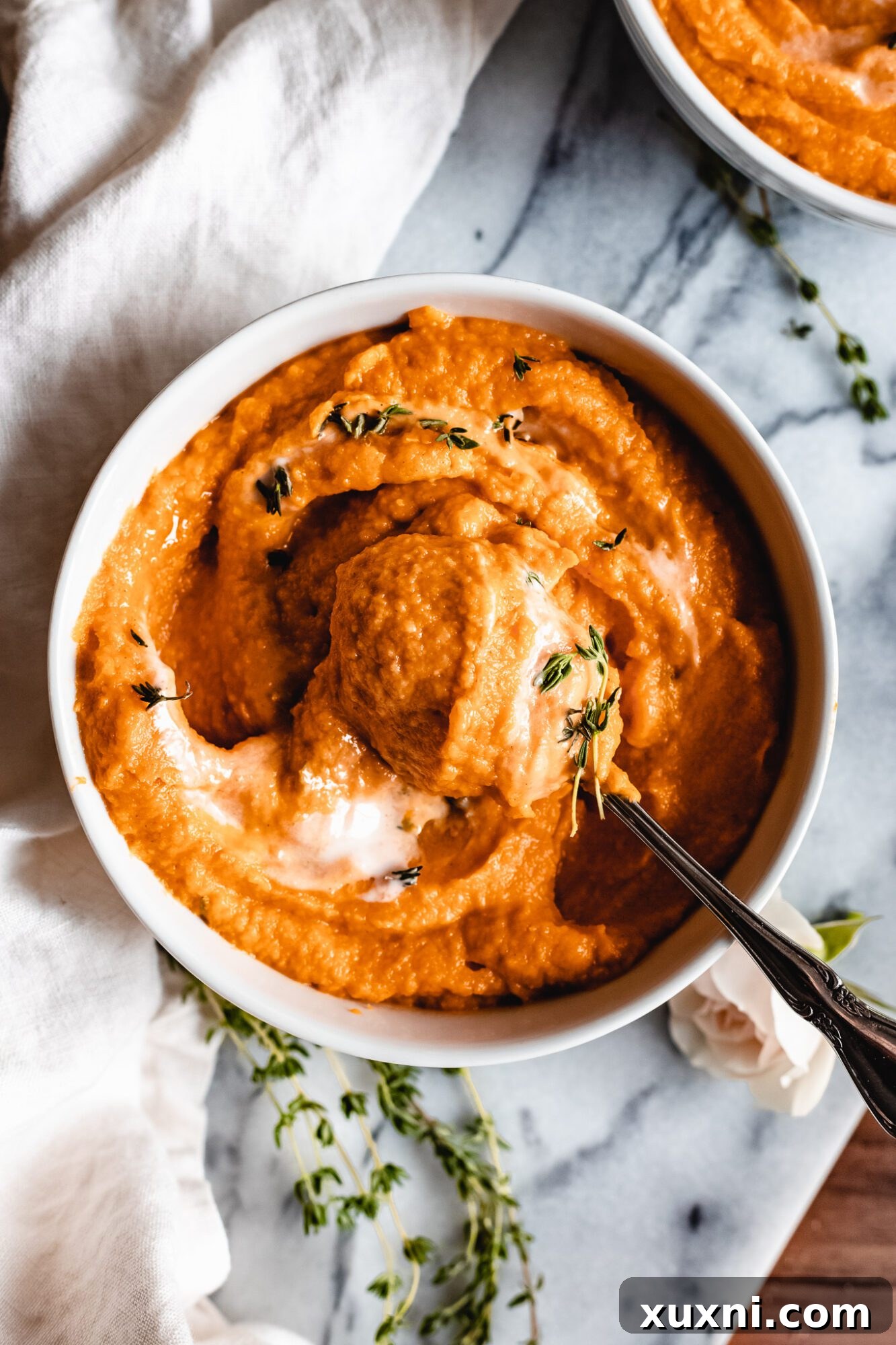 A spoon dipping into a bowl of rich, orange-hued sweet potato pumpkin soup, highlighting its thick and creamy texture.