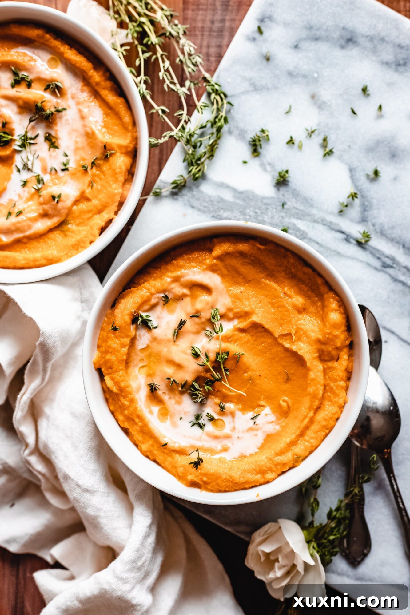 A bowl of pumpkin sweet potato soup garnished with fresh herbs and a drizzle of cream, sitting on a rustic marble slab.