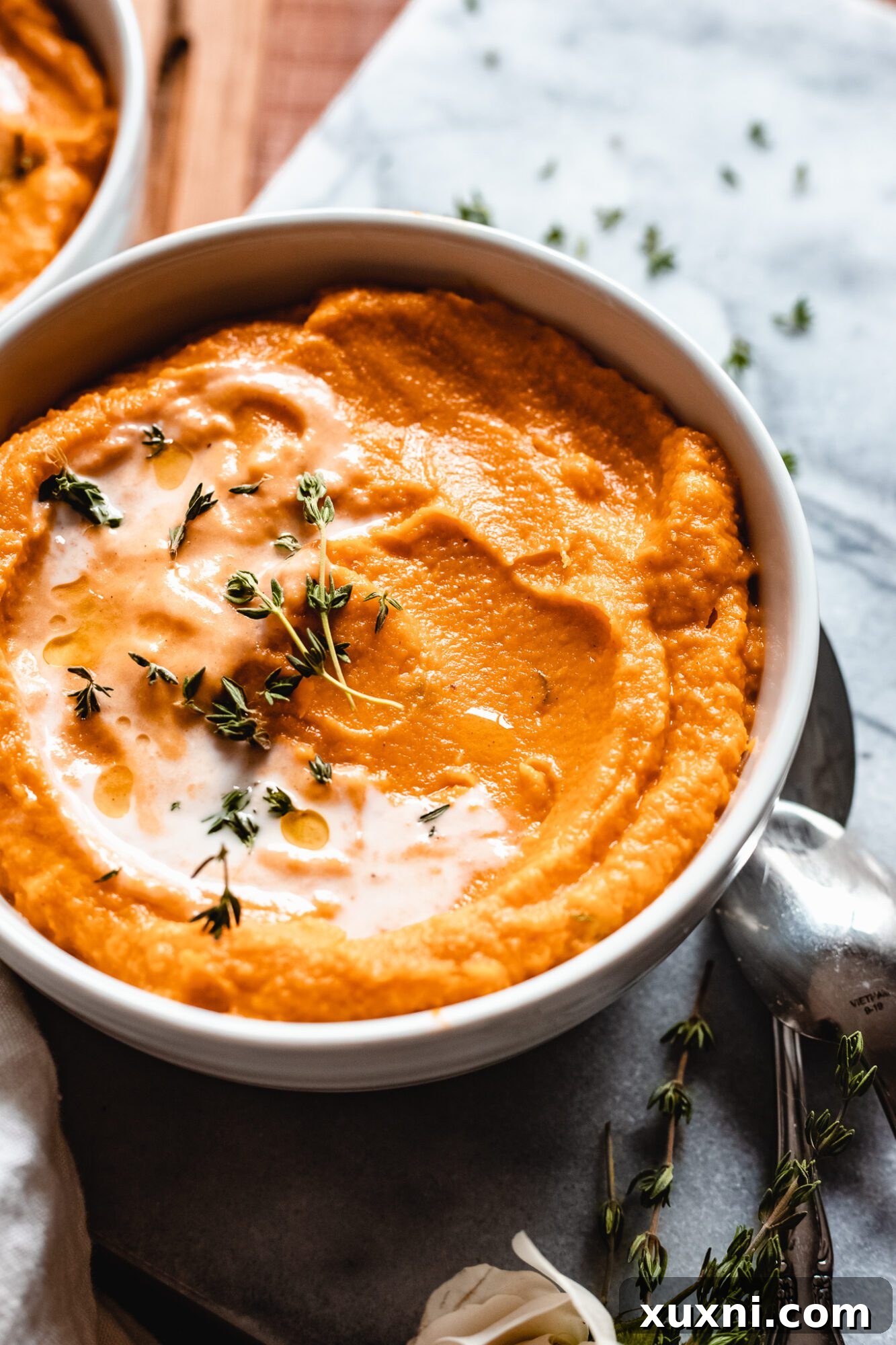 Close-up shot of the rich, orange color and creamy texture of vegan pumpkin sweet potato soup in a bowl.