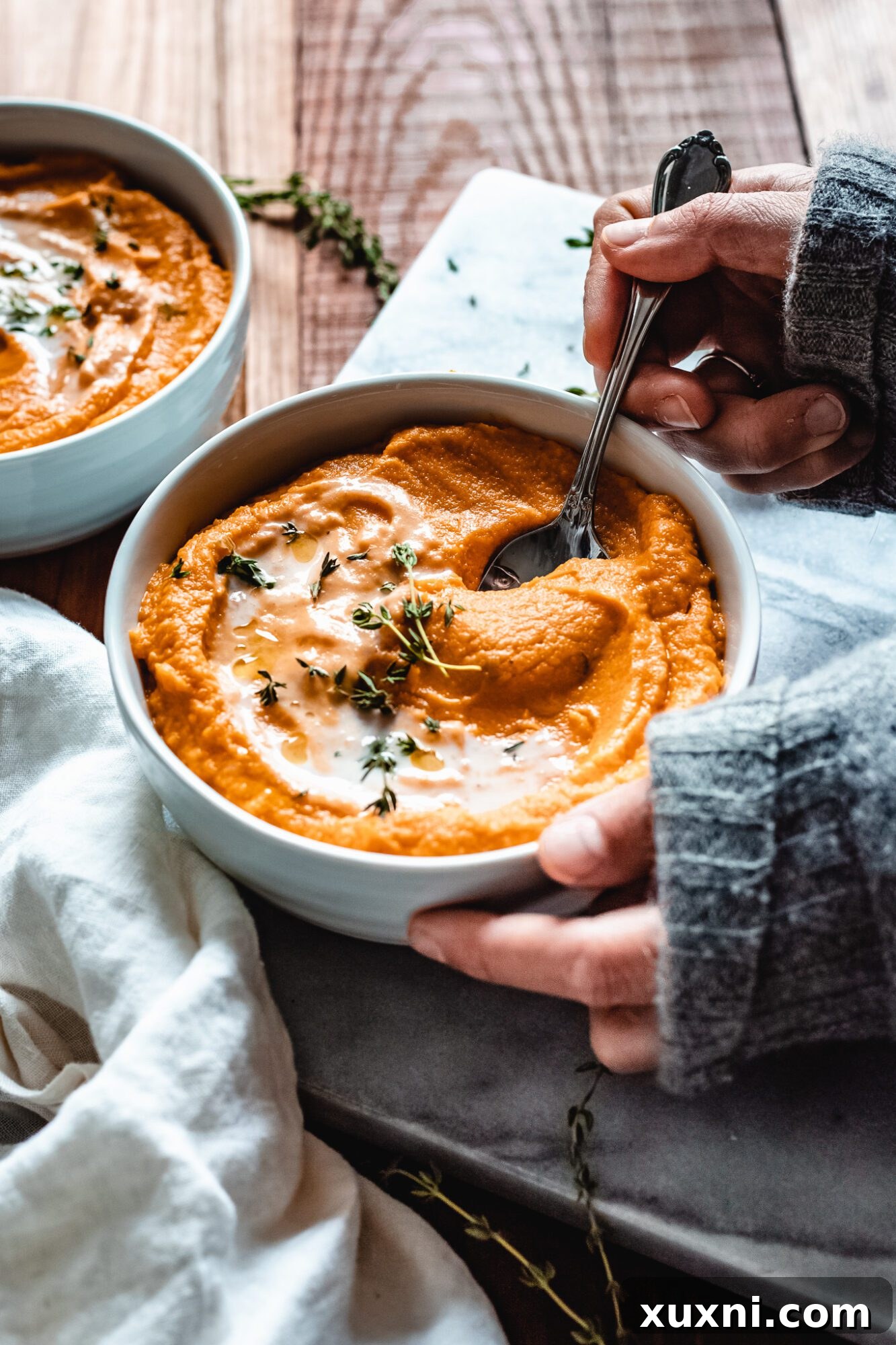 A hand reaching into a bowl of creamy pumpkin sweet potato soup with a spoon, ready to taste.