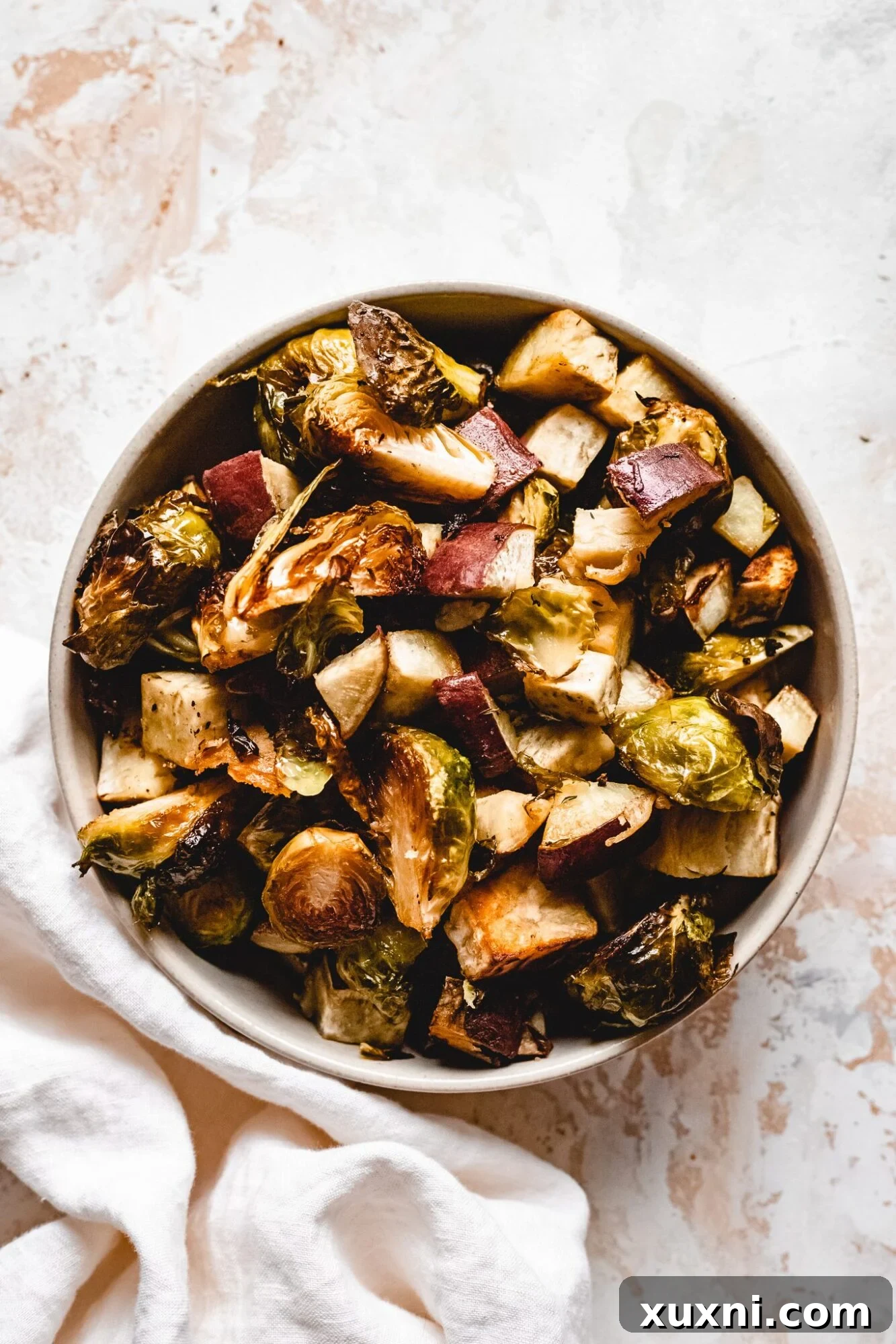 A beautifully presented bowl of crispy roasted potatoes and Brussels sprouts, ready to be served as a delicious vegan Thanksgiving side dish.