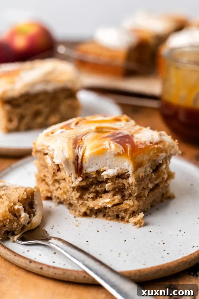 A beautiful slice of vegan apple spice cake on a pristine white plate, showcasing its soft texture, apple chunks, and rich caramel cream cheese frosting.