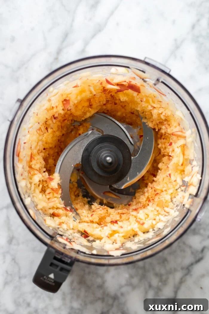 Finely blended apples in a food processor, creating a pulpy consistency ideal for even distribution in the cake batter.