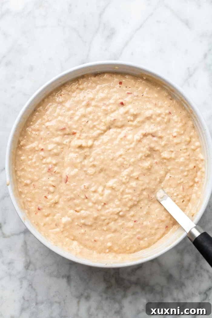 A large mixing bowl filled with smooth, golden apple spice cake batter, ready for baking.