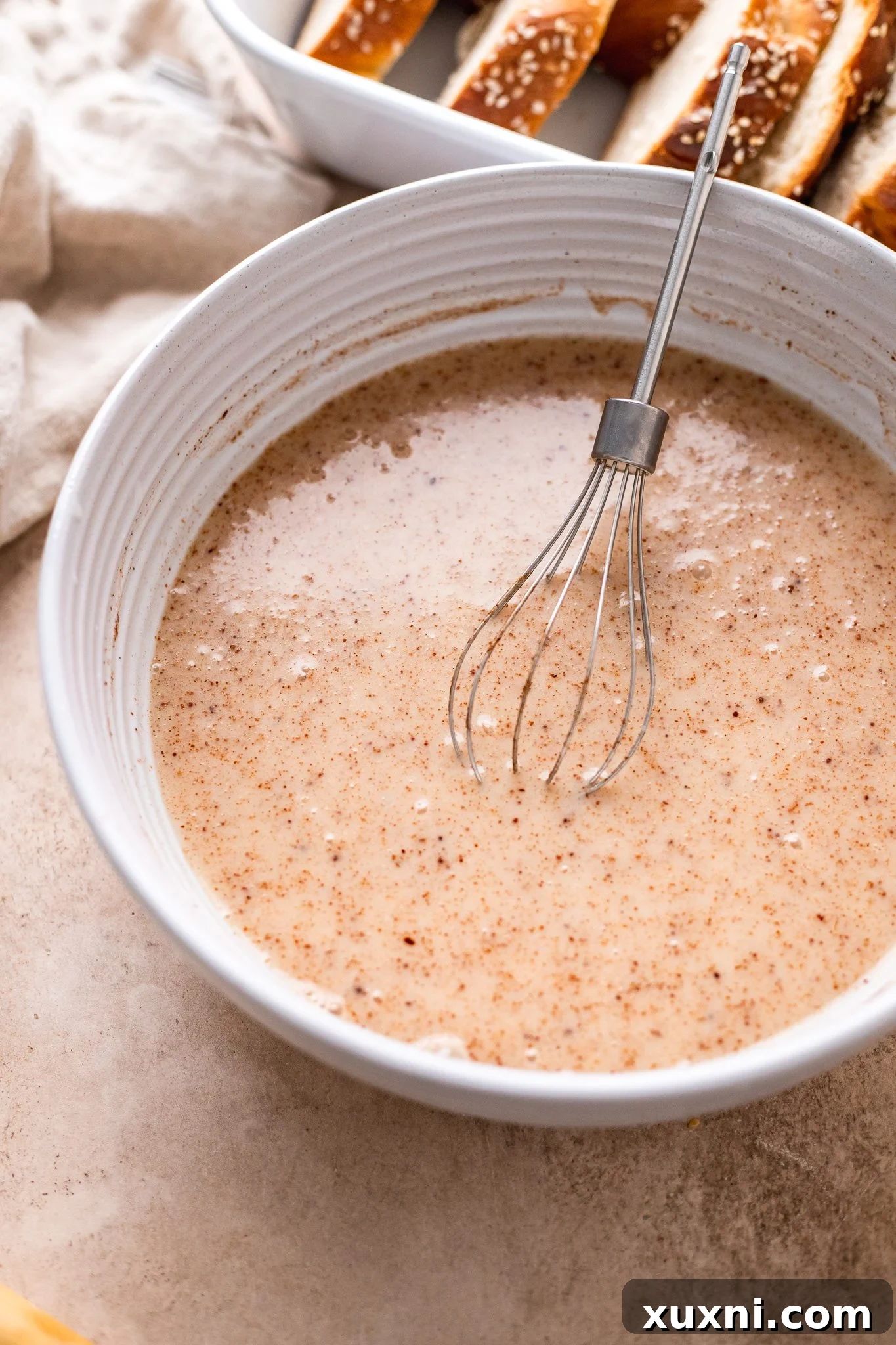 Close-up of the vegan French toast batter being poured over bread cubes in a dish.