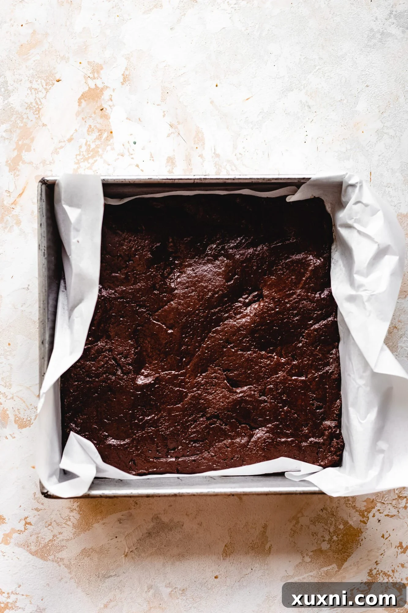 The smooth, dark vegan brownie layer spread evenly in a baking pan