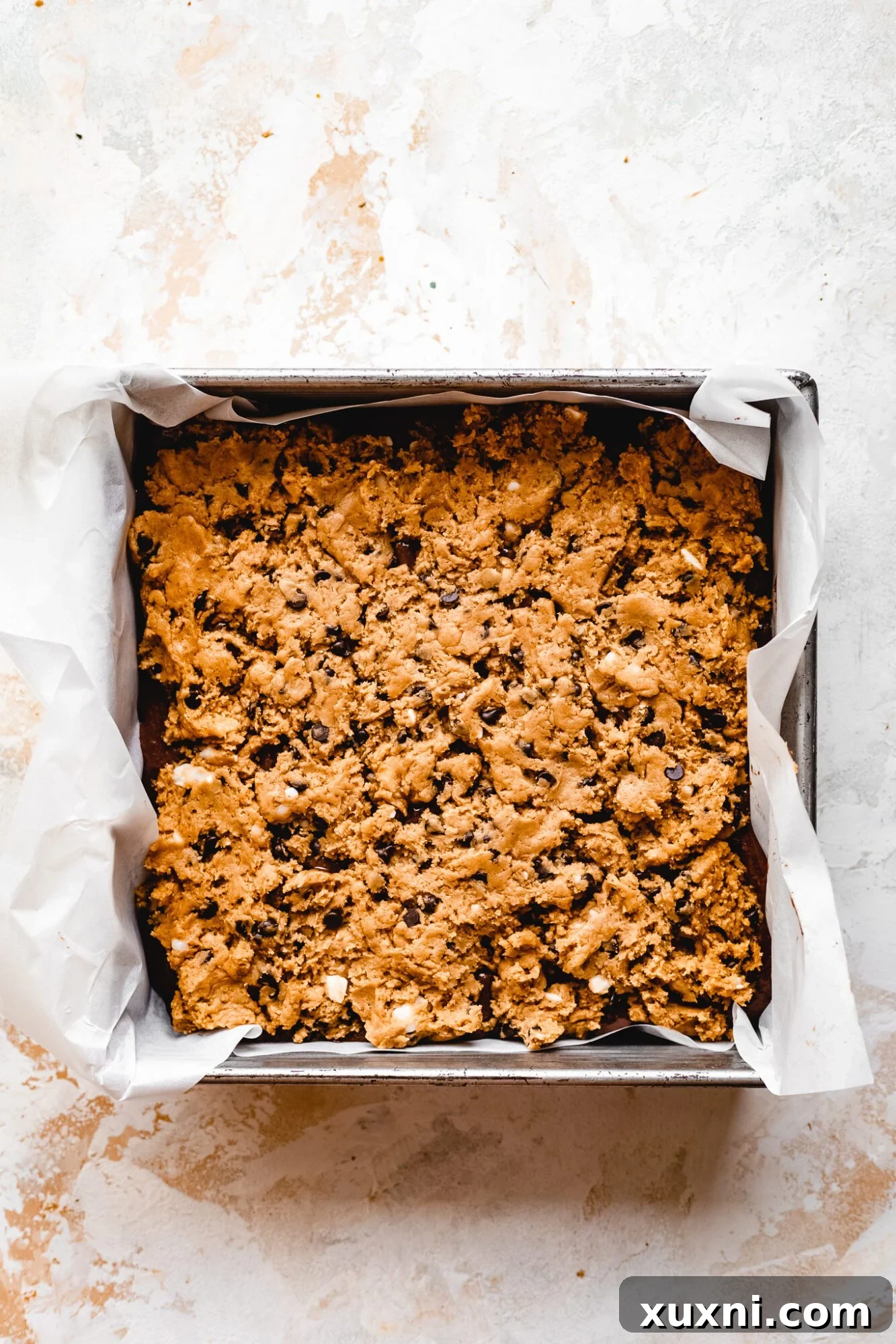 Unbaked vegan cookie dough layer evenly spread over the Nutella and brownie layers