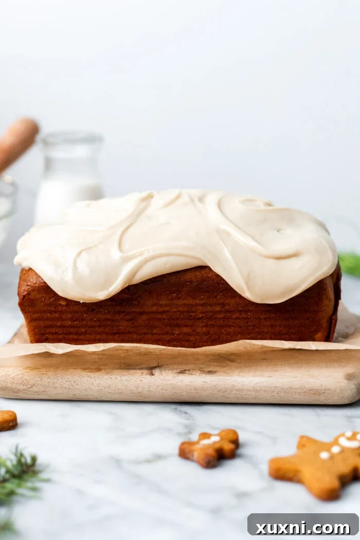 A glorious vegan gingerbread loaf cake, generously covered with a thick layer of creamy white cashew maple frosting, ready to be sliced and enjoyed.