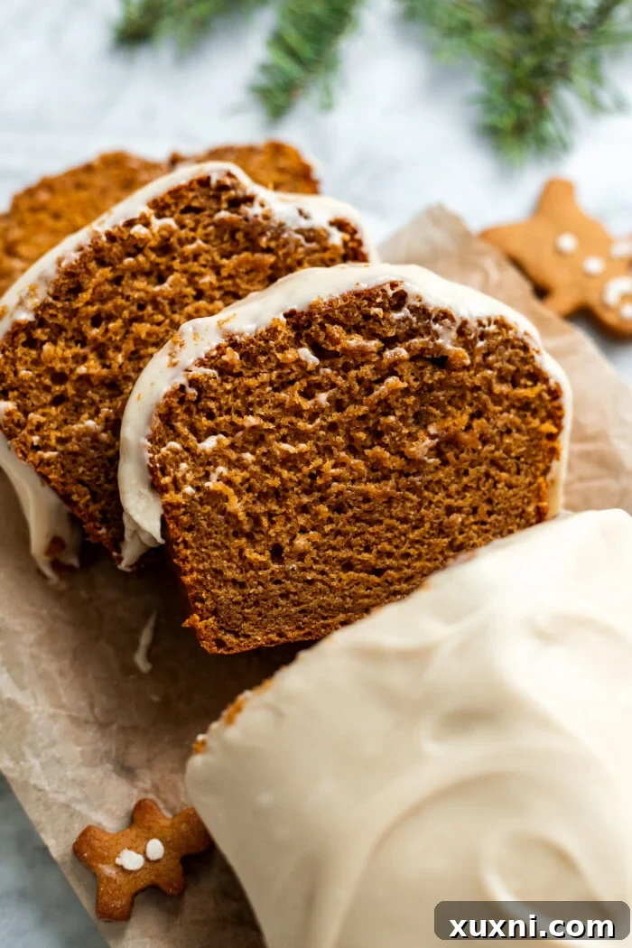 Two perfect slices of frosted vegan gingerbread loaf cake, showing off the fluffy texture of both the cake and the creamy cashew maple topping, on a clean white surface.