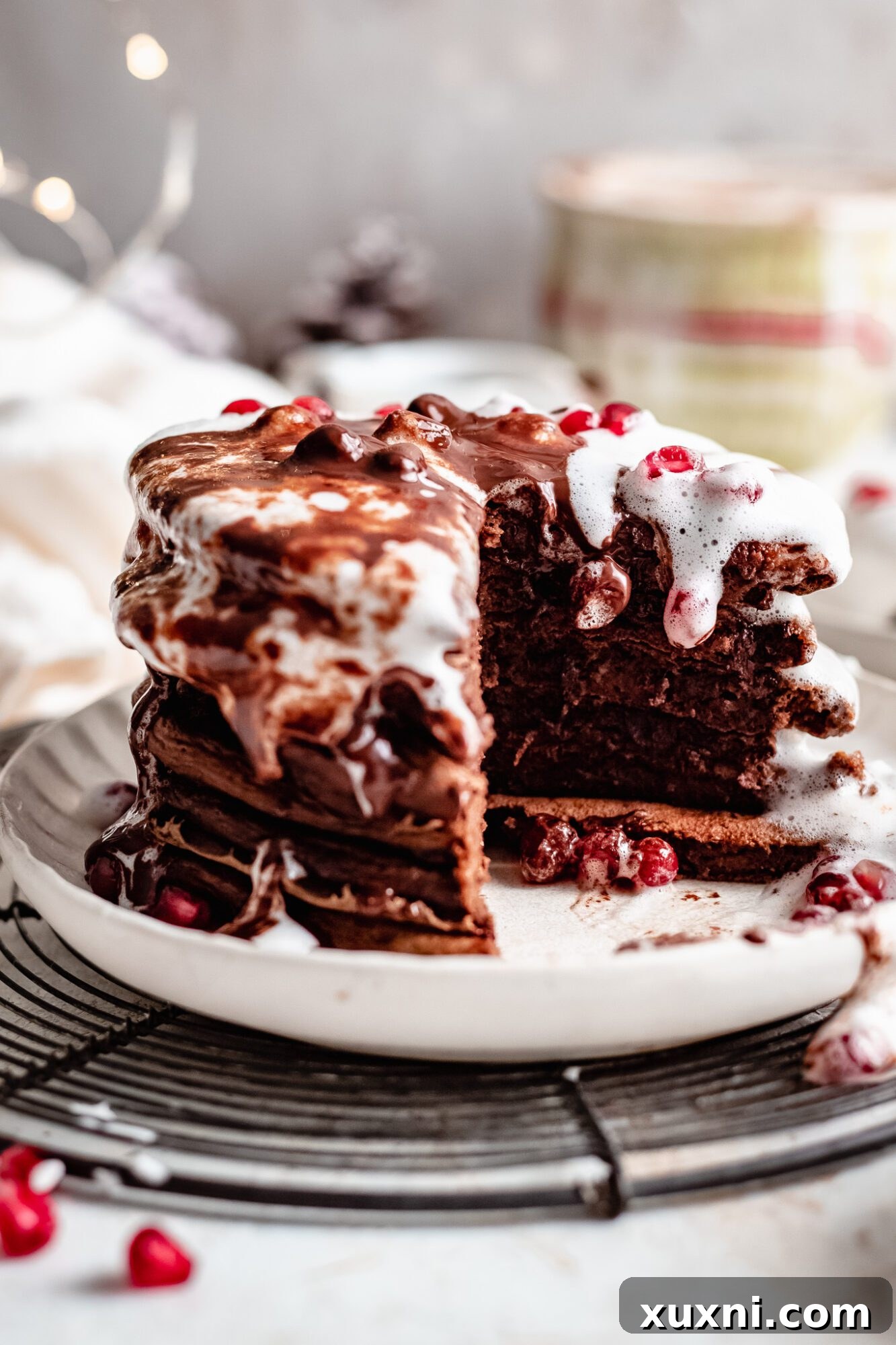 A stack of vegan chocolate pancakes topped with a variety of fruits and syrup.