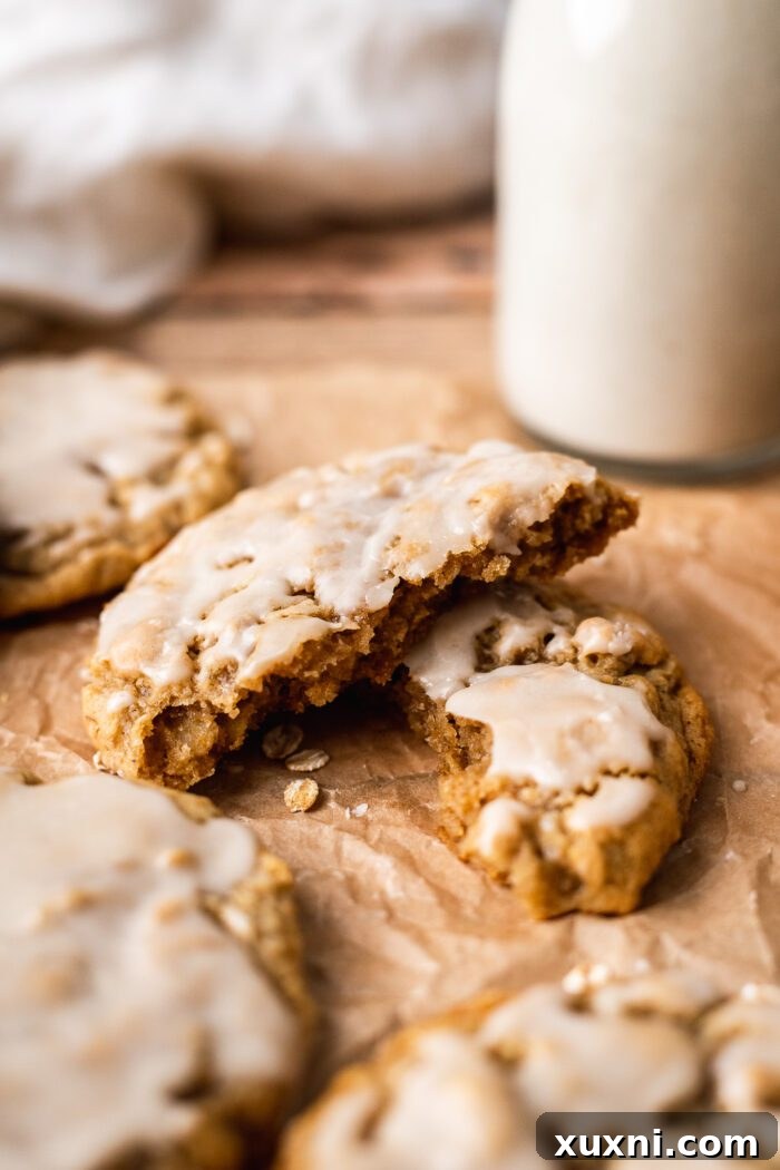 A freshly broken vegan oatmeal cookie revealing its soft, chewy interior, stacked on another whole cookie