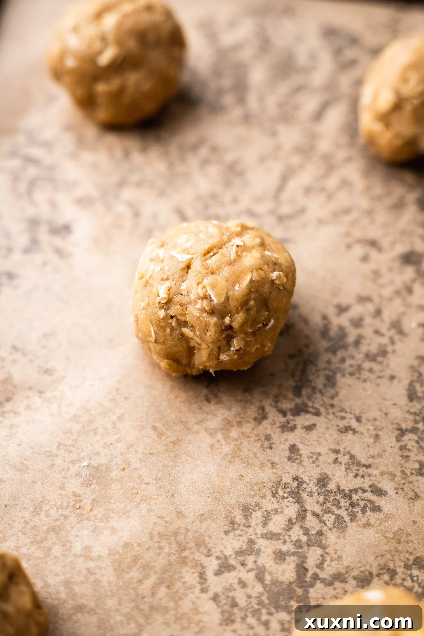 Unbaked vegan oatmeal cookie dough balls arranged on a parchment-lined baking sheet