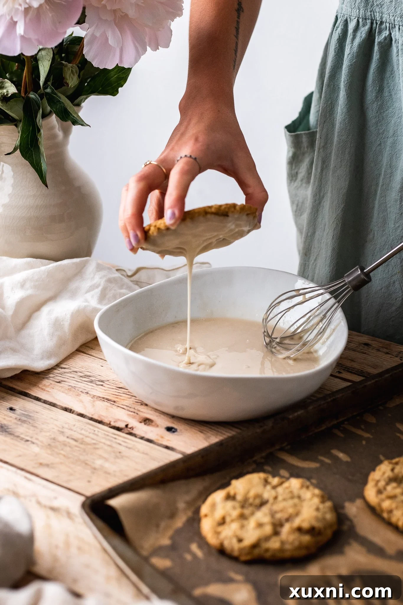 Dipping a baked vegan oatmeal cookie into a bowl of creamy white icing