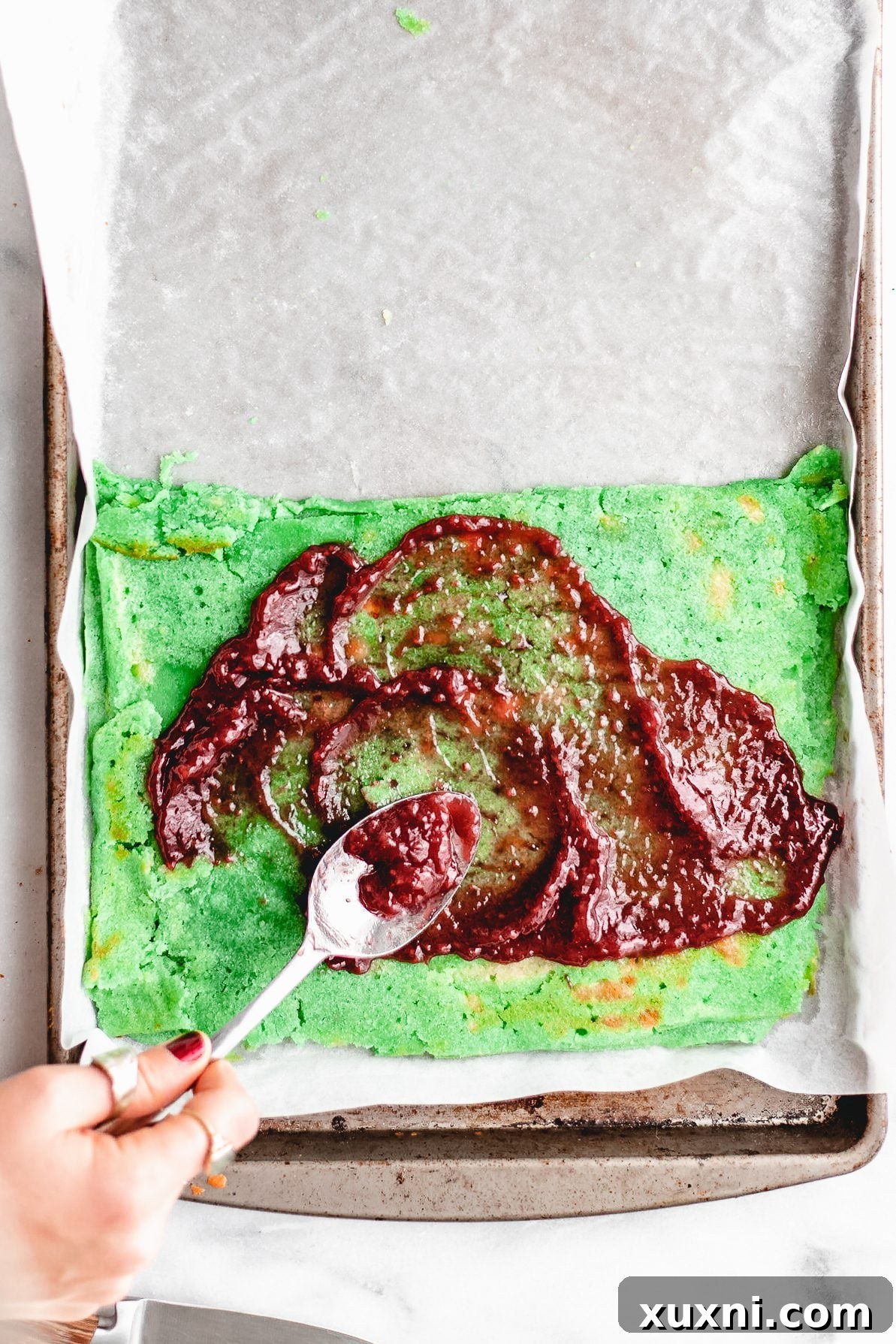 Raspberry jam being spread evenly on a cookie layer.