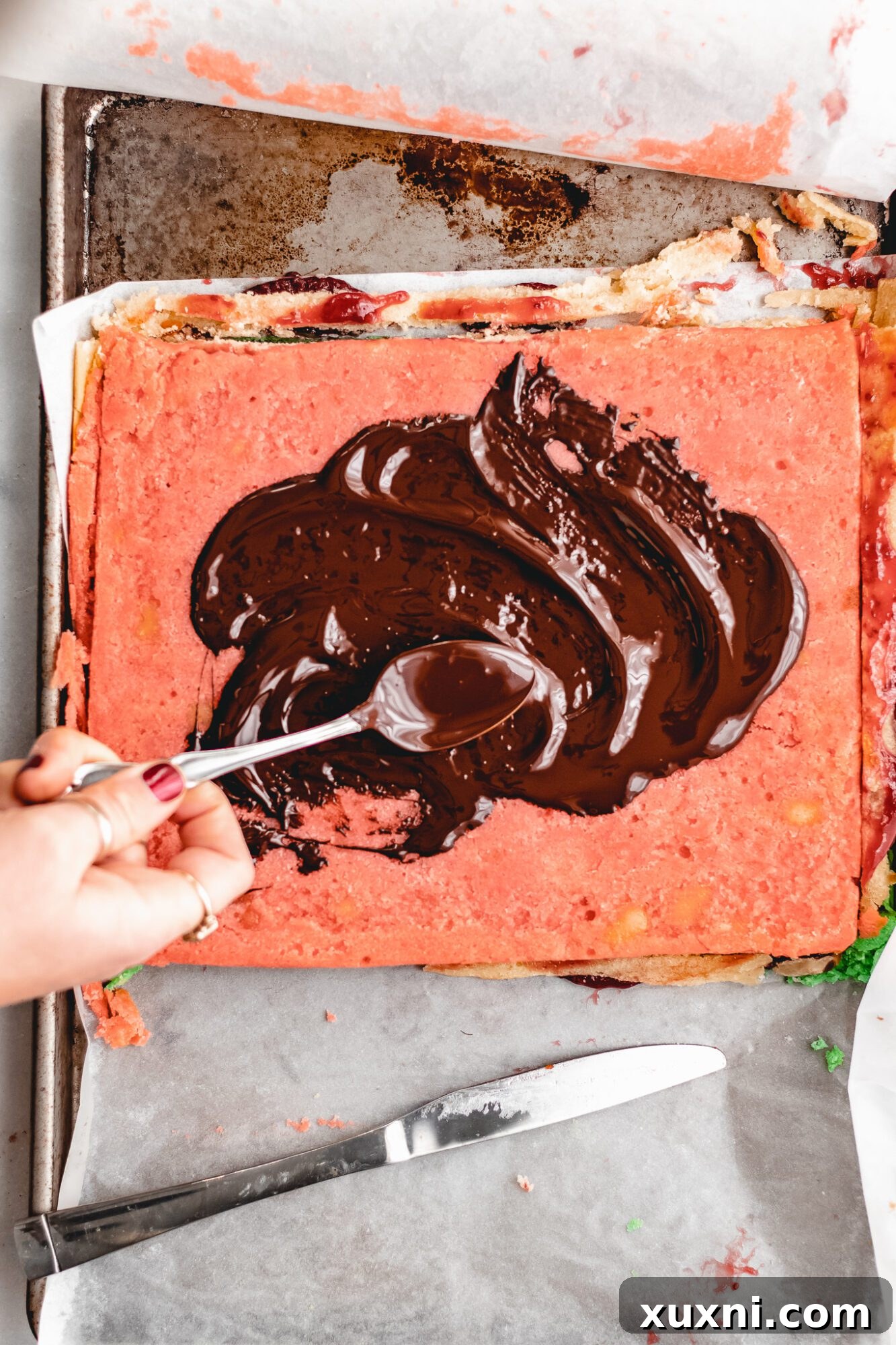 A hand spreading melted chocolate evenly over the top of the chilled cookie layers.