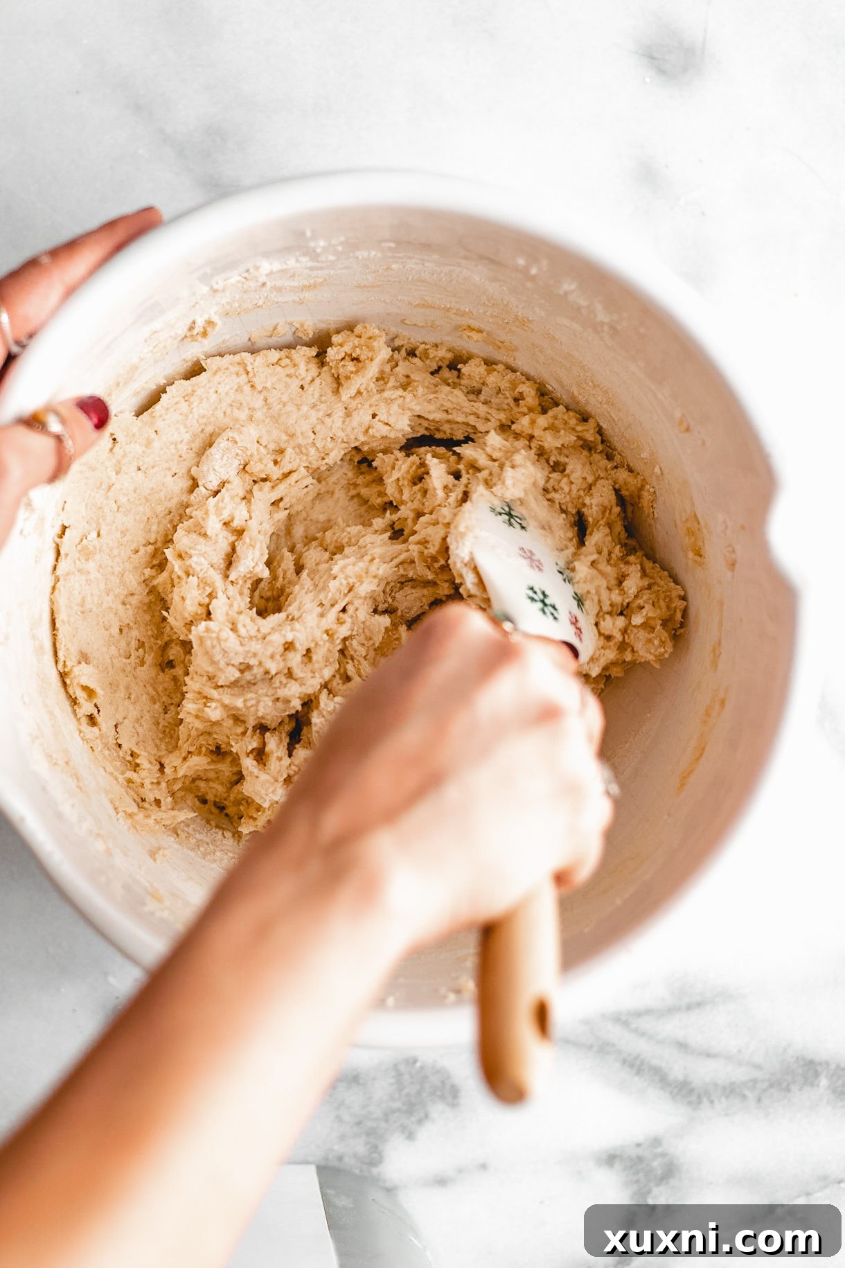 A hand mixing tricolor cookie dough to combine ingredients.