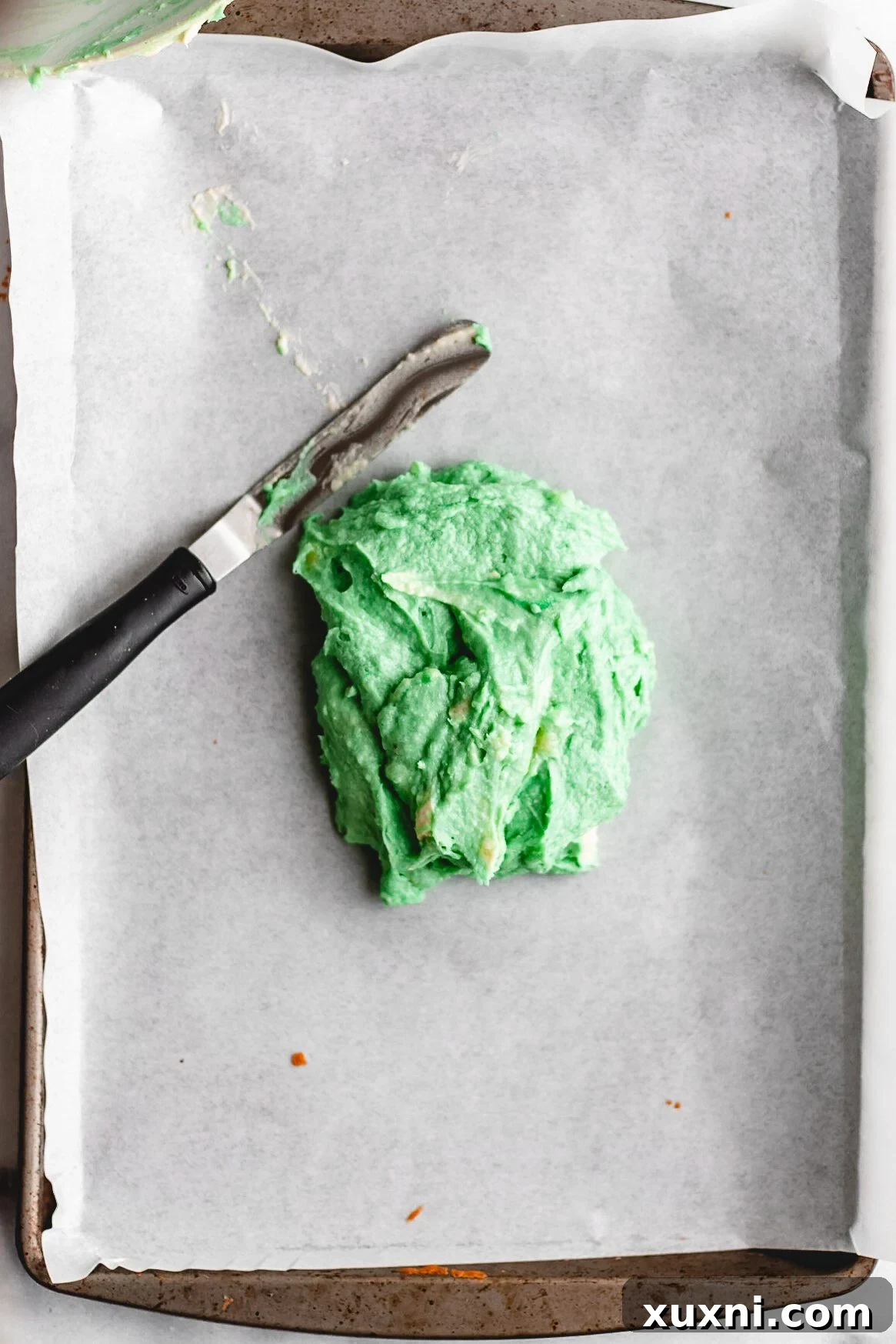 Cookie batter being spread thinly onto a parchment-lined cookie sheet.