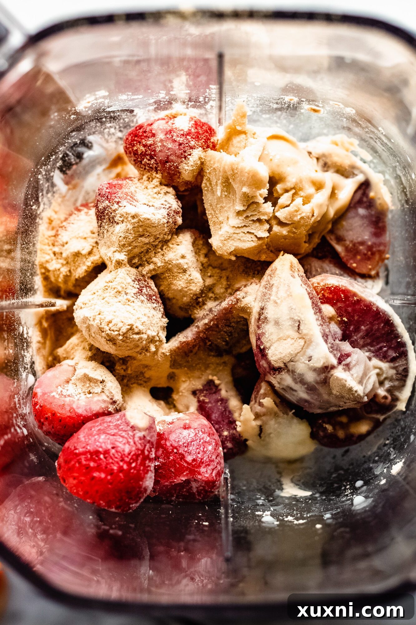 Blender filled with colorful strawberry orange smoothie ingredients before blending