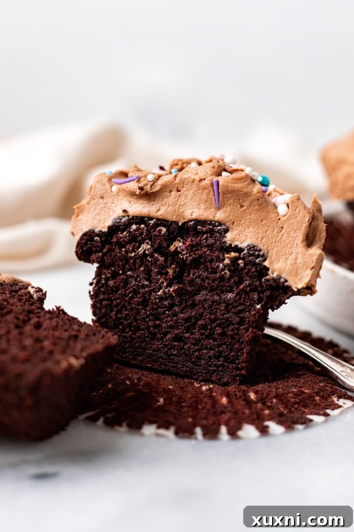 A perfectly baked vegan chocolate cupcake sliced in half, showcasing its incredibly moist and rich interior, ready to be enjoyed.