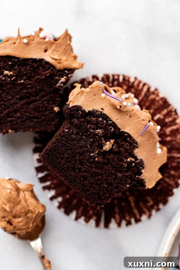 A vegan gluten-free chocolate cupcake, elegantly sliced open, revealing its moist and tender crumb topped with chocolate sour cream buttercream and colorful sprinkles.